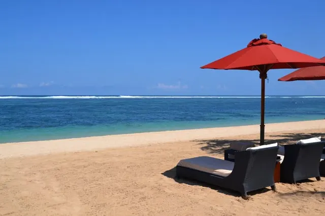A red umbrella and loungers on the white sand at Nusa Dua, blue sky
