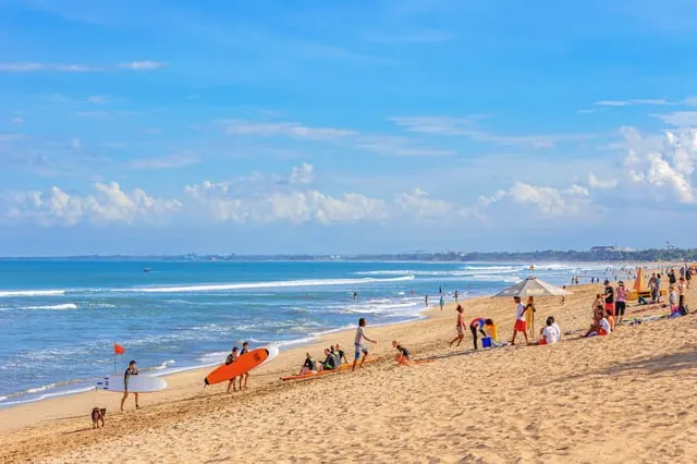 The busy sand and surf of the Kuta-Legian beach under a blue sky (people on the beach)