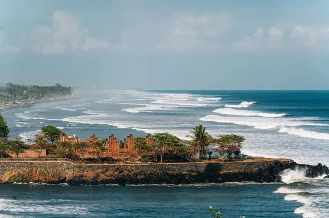 Surf and a coastal temple on Bali's Tabanan coast, blue sky (stand-in: not confirmed as Pasut)