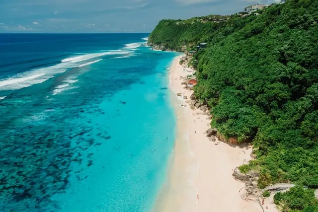 Aerial view of a white beach, turquoise sea and jungle cliffs in Bali