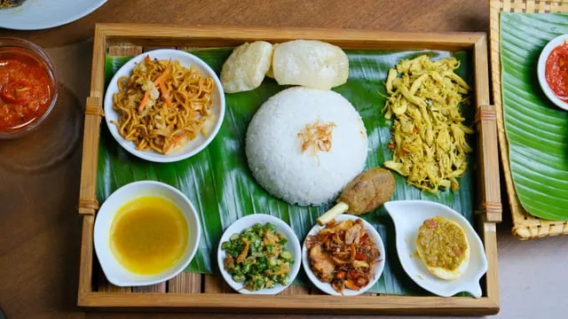 A nasi campur tray with rice and many small dishes on banana leaf