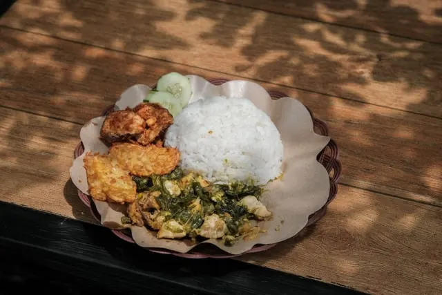 Balinese chicken rice with vegetables and crispy chicken on a paper-lined plate