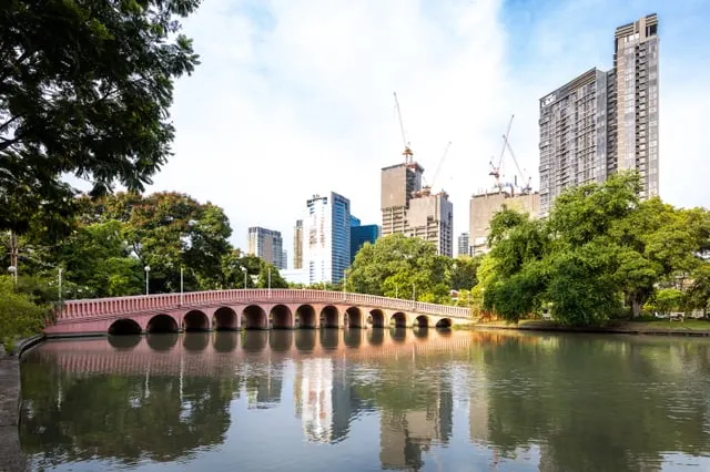 The arched bridge over Chatuchak Park's lake, towers behind, sunny