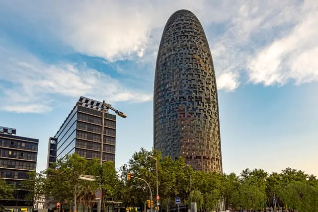 Torre Glòries against a blue sky with clouds