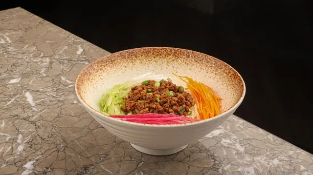 Dan dan noodles topped with crumbled filling and greens