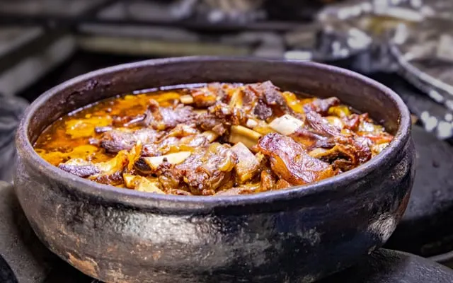 Slow-cooked meat stew with bones in a rustic dark clay pot