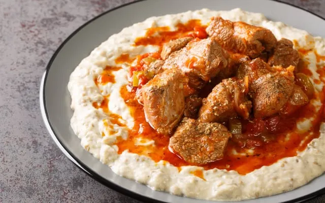 Stewed meat pieces in tomato sauce served over creamy smoked aubergine purée
