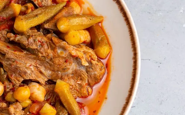 Close view of a stew of meat, okra and chickpeas in tomato sauce in a rimmed bowl