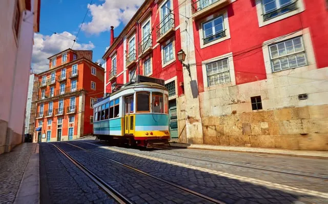 Image licensed from Shutterstock A yellow and turquoise tram on a cobbled street between red and orange houses in Lisbon