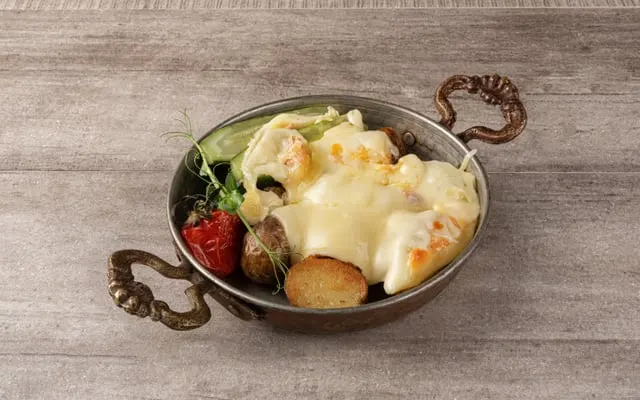 Melted cheese over potatoes and vegetables in a small copper pan
