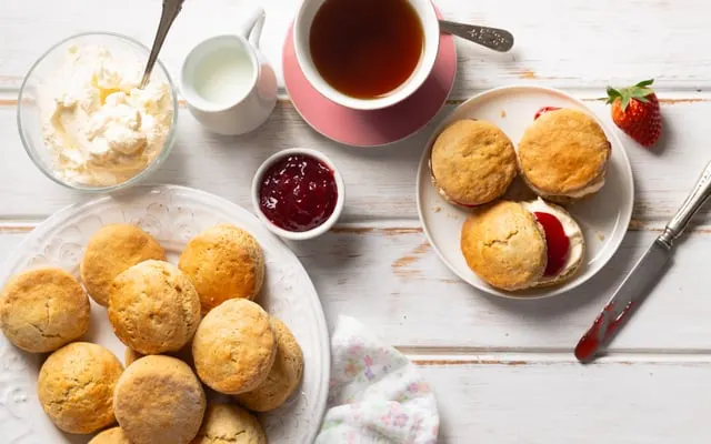 Scones with jam and clotted cream, a pot of milk and a cup of tea on a white table