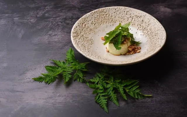 Small herb-topped dish in a speckled bowl, with fern leaves on a dark surface