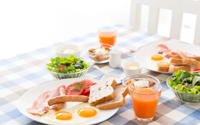 Breakfast table with fried eggs, toast, salad, juice and cereal on a checked cloth