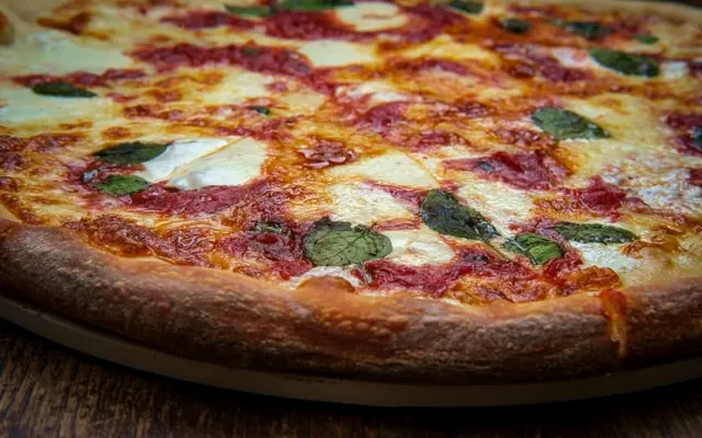 Close view of a whole pizza with tomato sauce, melted mozzarella and fresh basil leaves