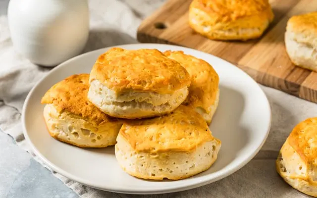 Plate of golden baked biscuits on a table with a wooden board and more biscuits behind