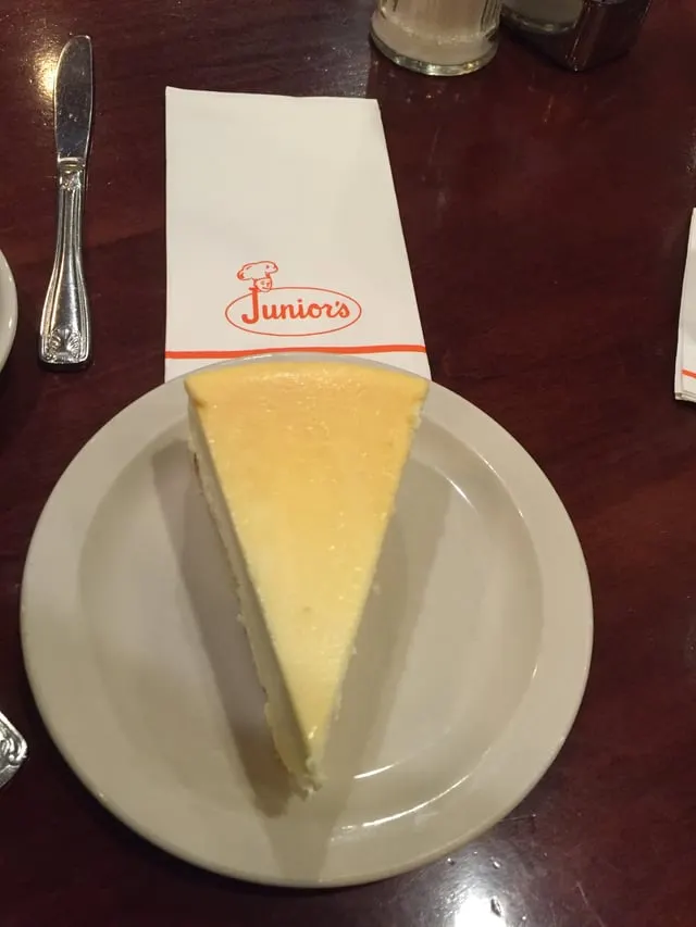 A slice of New York-style cheesecake on a plate beside a Junior’s napkin