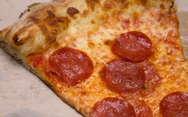 Close view of a pizza slice with melted cheese, tomato sauce and round red meat slices on paper