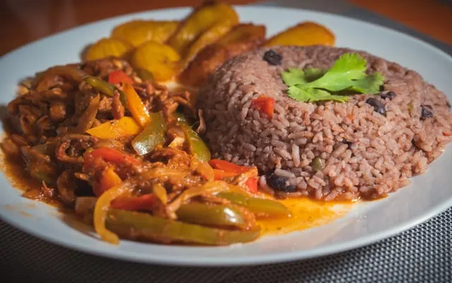Plate of rice with black beans, a pepper and onion stew and fried plantain slices, topped with coriander