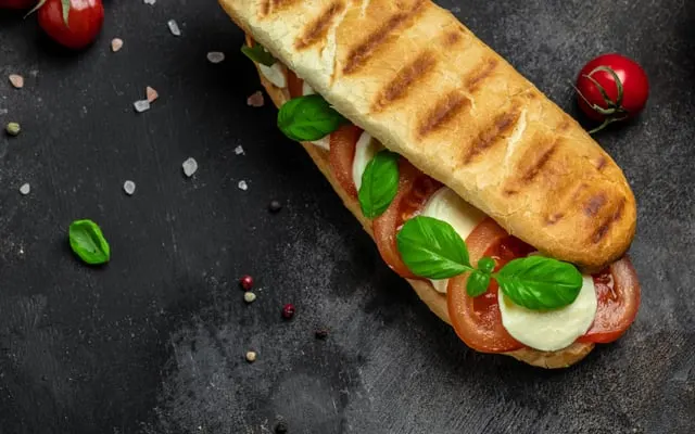 Grilled panini with sliced tomato, fresh mozzarella and basil on a dark surface