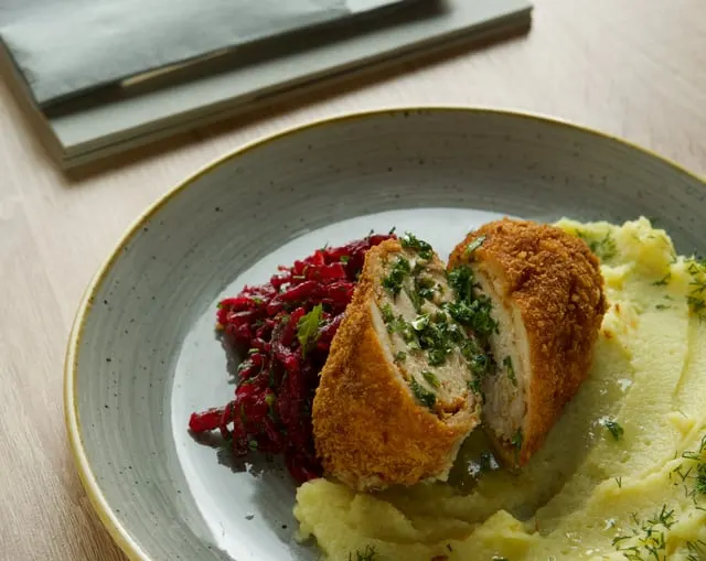 Chicken Kyiv cut open to show the herb butter, with mash and salad